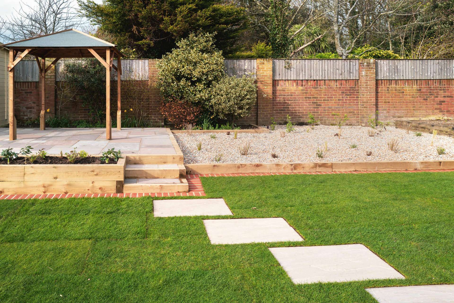 Trittsteine und Stufen aus Natursteinplatten führen zu erhöhten Terrasse im Garten.